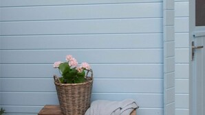 A corner of a room with a light blue wall, a wicker basket with pink flowers, and a wooden bench. - Spacious Holiday Home in Oostkapelle (Oostkapelle)