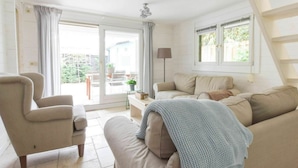 A living room with a sofa, armchair, and a table with a lamp. There is a sliding glass door leading to an outdoor area with a patio and a view of greenery. - Spacious Holiday Home in Oostkapelle (Oostkapelle)