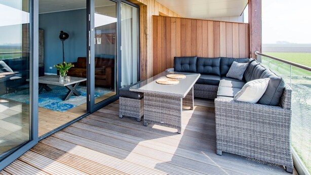 A modern outdoor living area with a sofa, two wicker chairs, a coffee table, and a floor lamp. - Holiday Home in Kamperland (Kamperland)