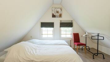 A bedroom with a sloped ceiling, a bed, a chair, a radiator, and a window with a curtain.