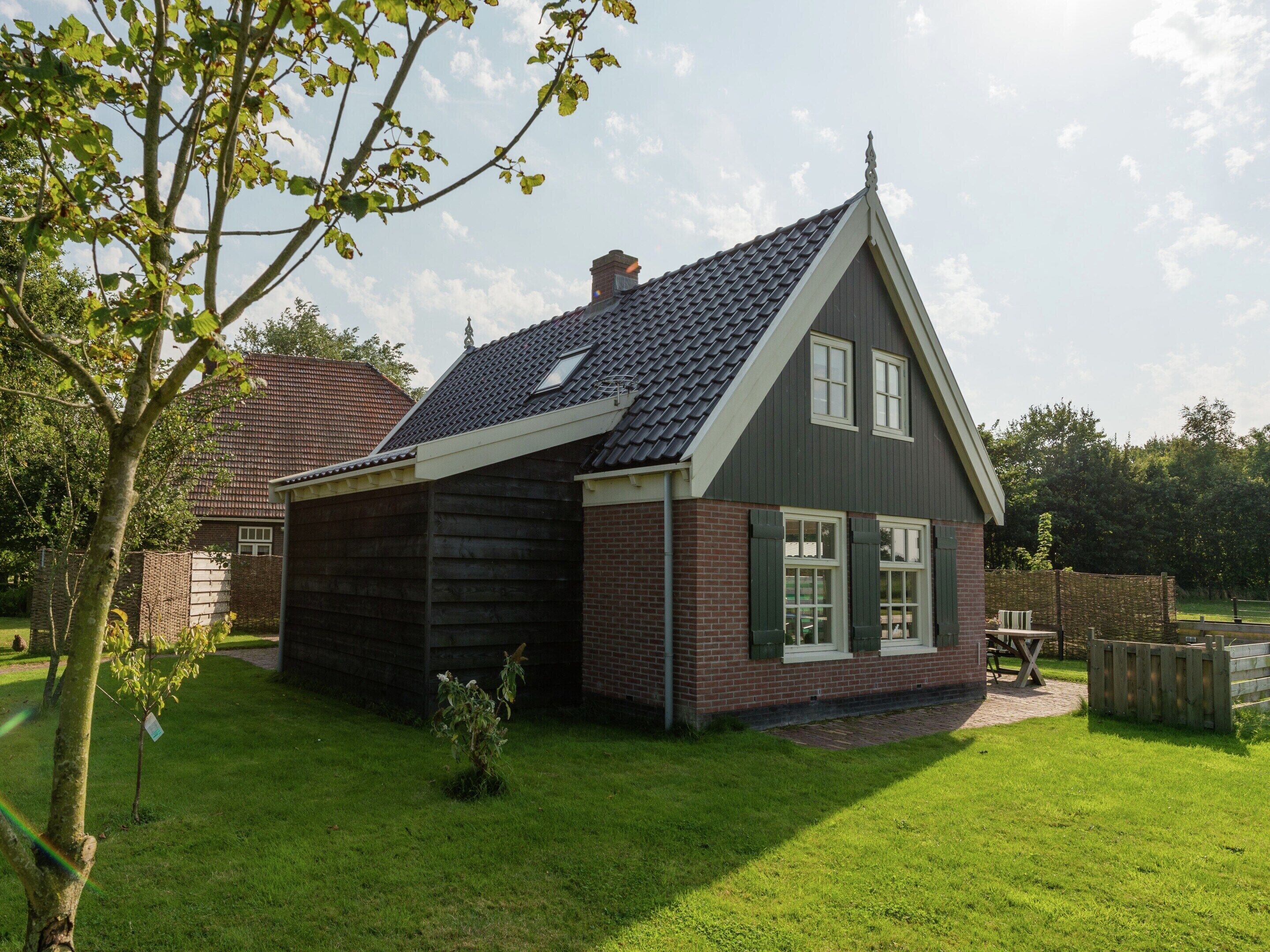 A two-story house with a sloped roof, brick exterior, and a small front yard with a tree and a bench.