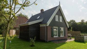 A two-story house with a sloped roof, brick exterior, and a small front yard with a tree and a bench.