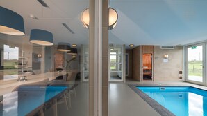 Ein modernes Hallenbad mit großen Glaswänden, einer Bar und Blick ins Freie.