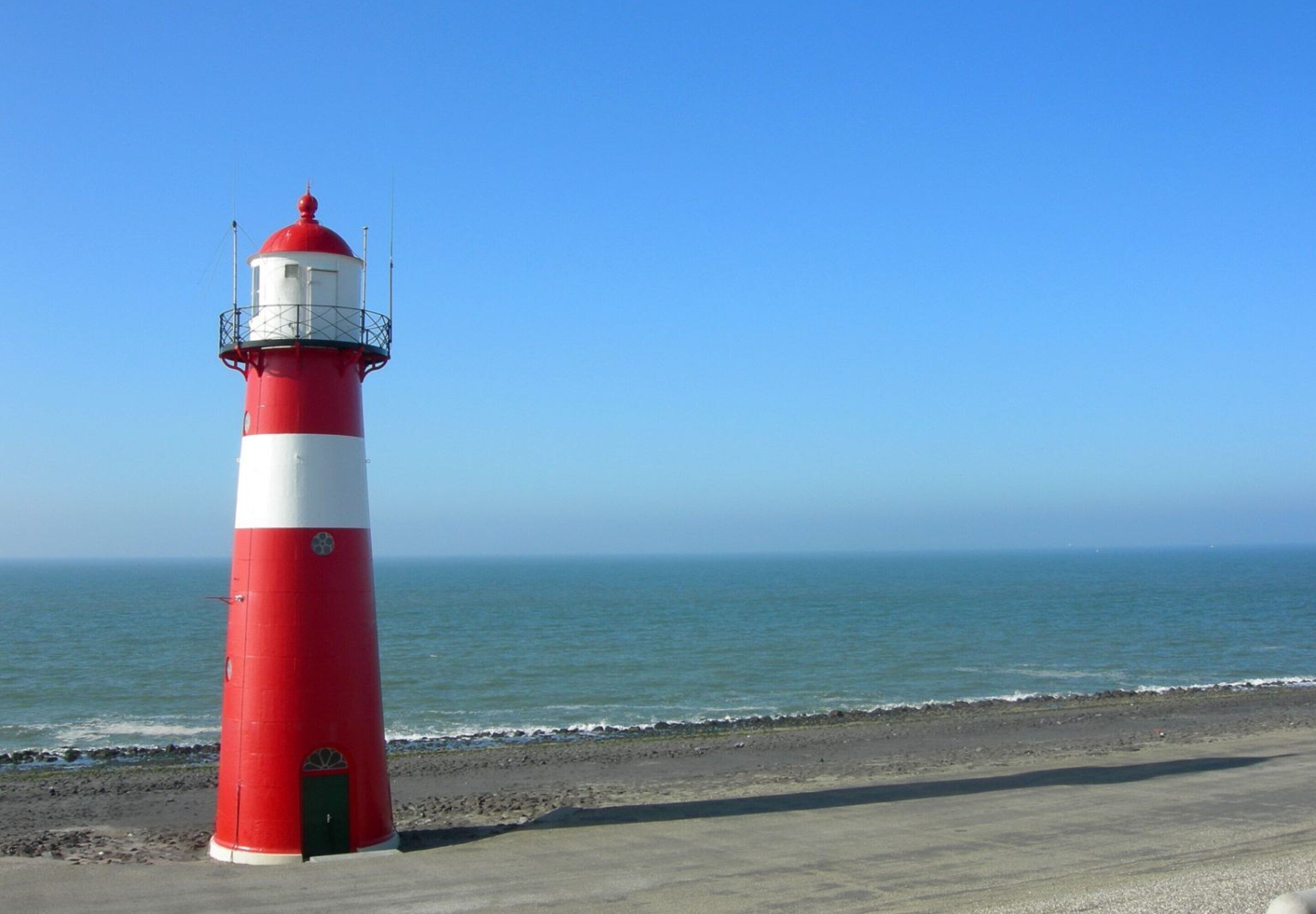 A red and white lighthouse on a beach with the ocean in the background.