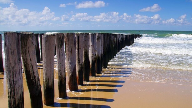Eine Holzsteg, der sich ins Meer erstreckt, wo Wellen aufschlagen.