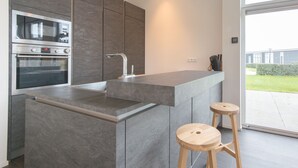 A modern kitchen with a built-in oven, a stainless steel sink, and a large island with stools. - Modern Chalet Near Beach (Wemeldinge)