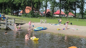 A lakeside setting with a wooden dock, inflatable rafts, and people engaging in water activities. - Cozy House near River (Notter)