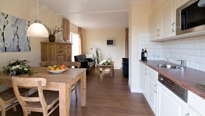 A modern kitchen with white cabinets, a stainless steel sink, and a wooden dining table with chairs. - Cozy House near River (Notter)