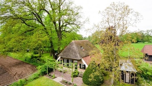 A traditional house with a thatched roof, surrounded by lush greenery and a well-maintained garden. - Cozy House near River (Notter)