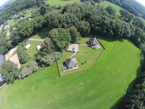 Vista aérea de una propiedad rural con varias casas, un campo verde extenso y abundante vegetación.