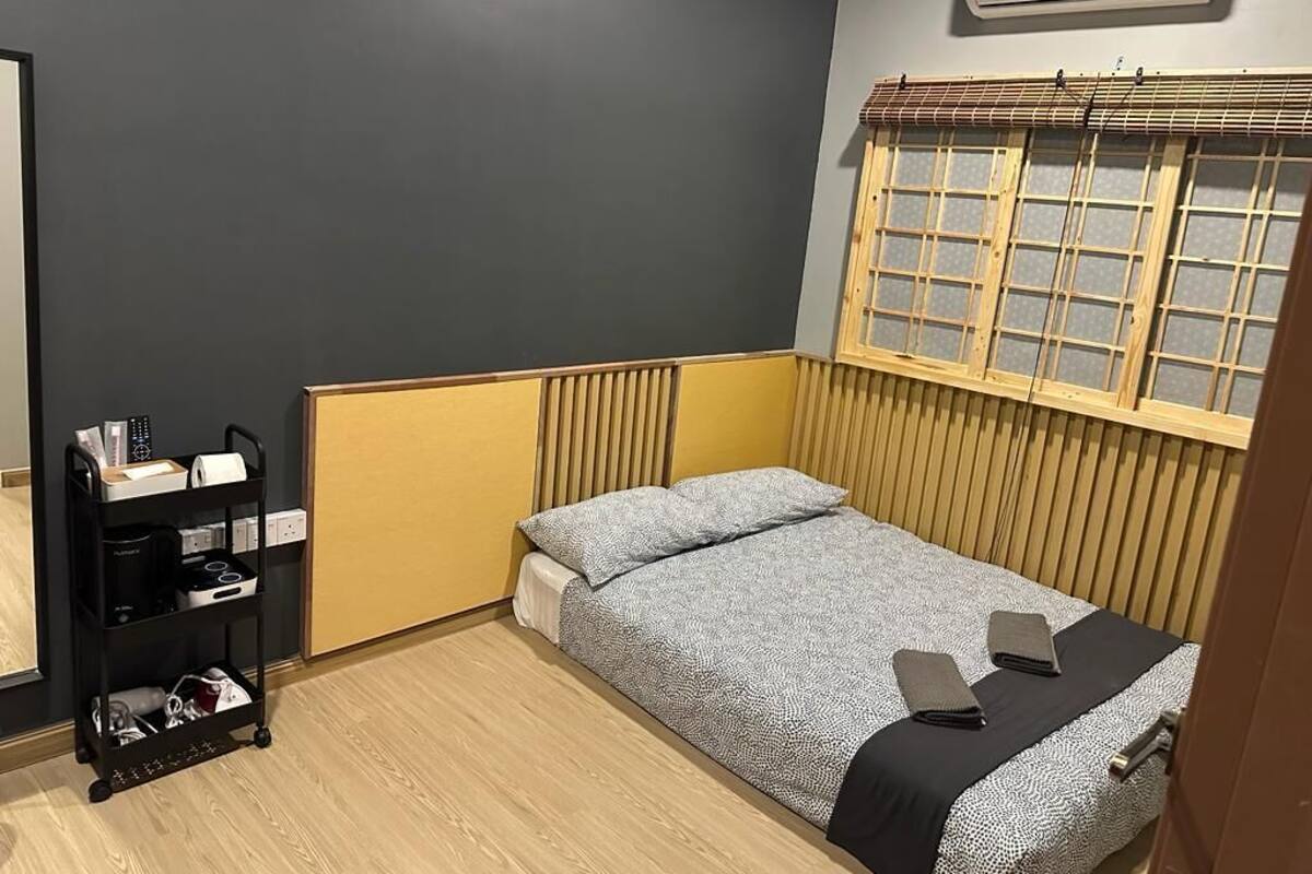 Een kleine kamer met een enkel bed, een klein schap en een raam met zonwering.