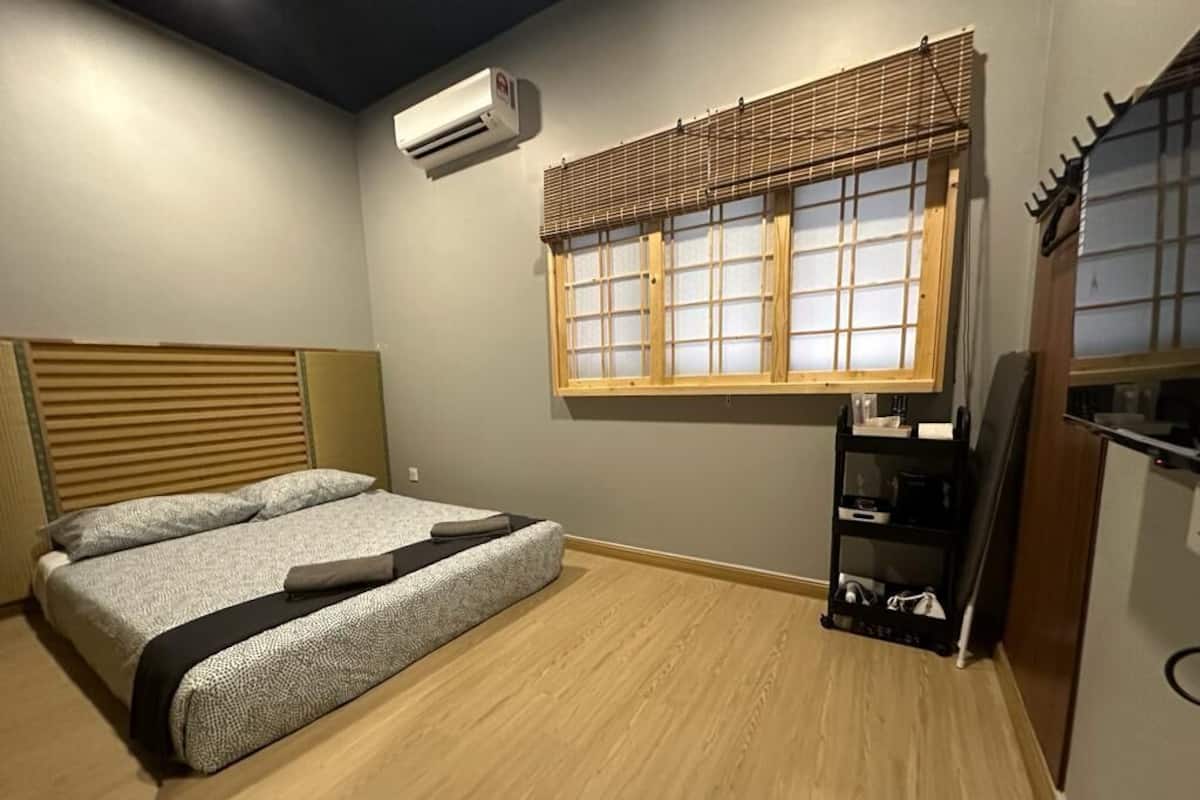 Een slaapkamer met een bed, een raam met houten jaloezieën, een plank met spullen en een aan de muur bevestigde airconditioner.