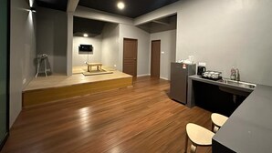 Een ruime kamer met houten vloer, een klein podium, een televisie en een kitchenette.