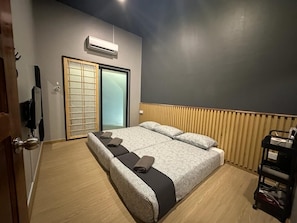 A hotel room with a large bed, a sliding door, an air conditioning unit, and a wooden floor.