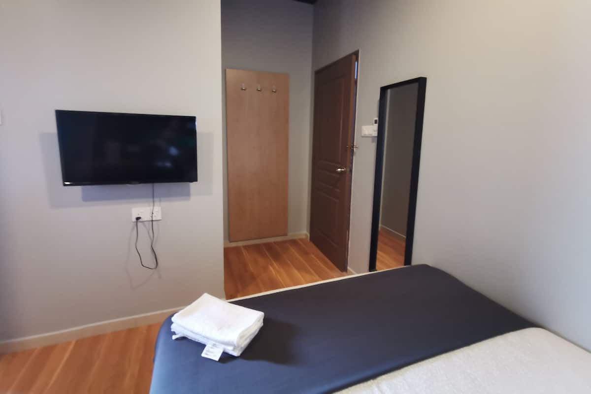 Een slaapkamer met een bed, een aan de muur bevestigde televisie, een houten deur en een kledingkast.