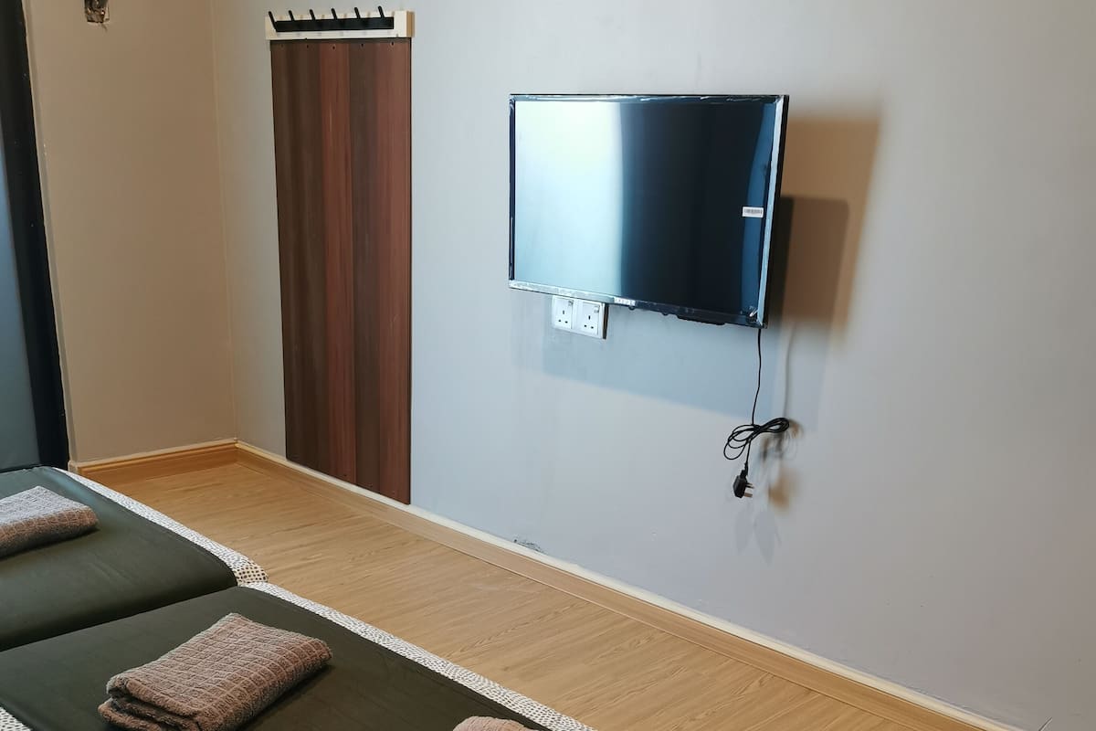 Een kamer met een bed, een aan de muur bevestigde televisie en een houten vloer.