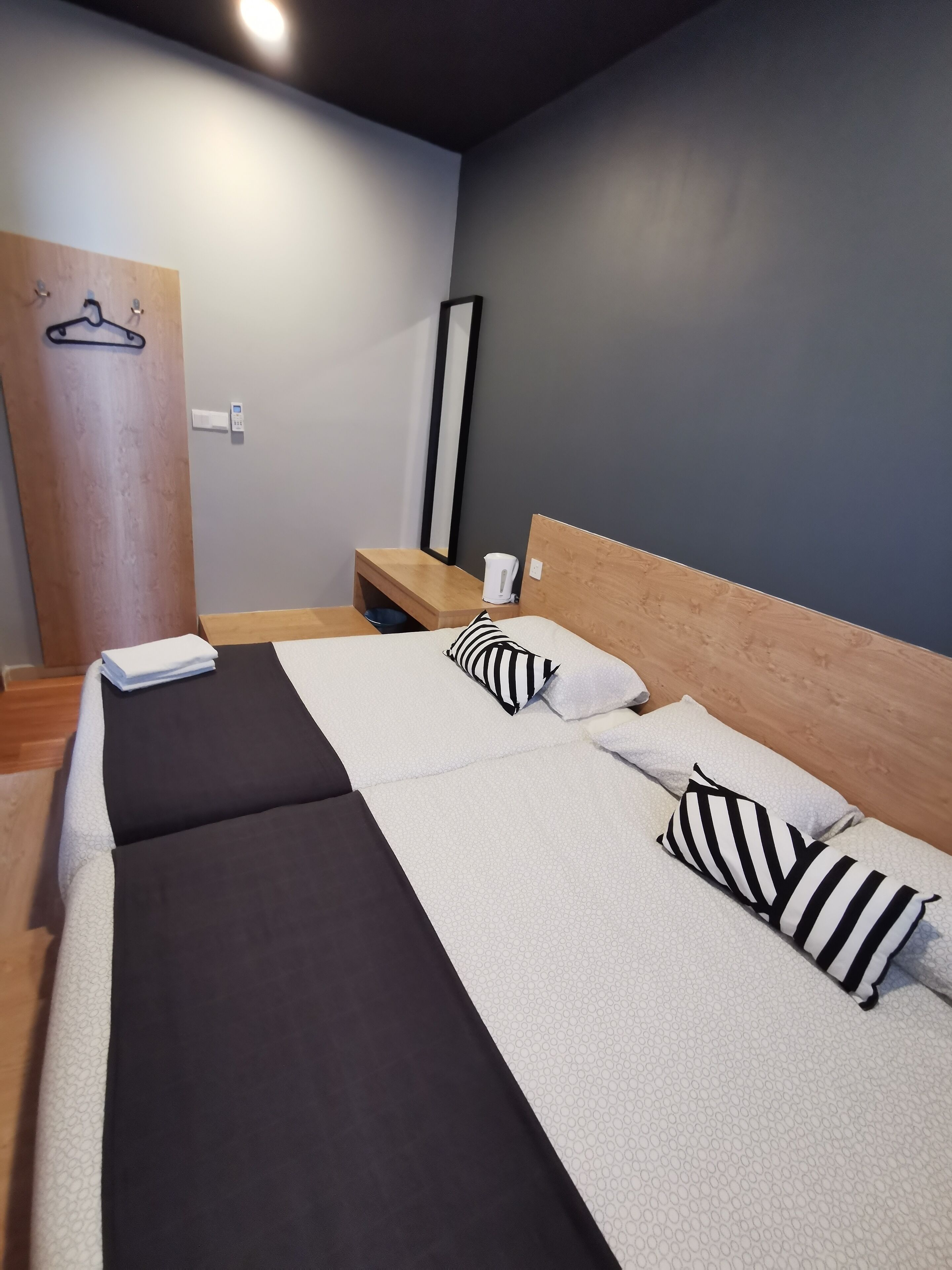 A neatly made bed with striped pillows, a wooden headboard, and a bedside table with a kettle.