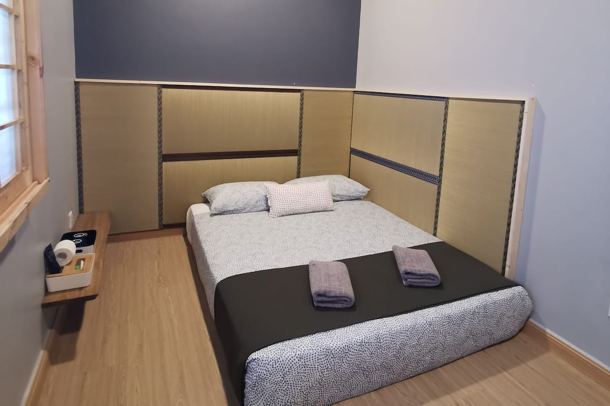 Een slaapkamer met een bed, nachtkastje, raam en een airconditioning.