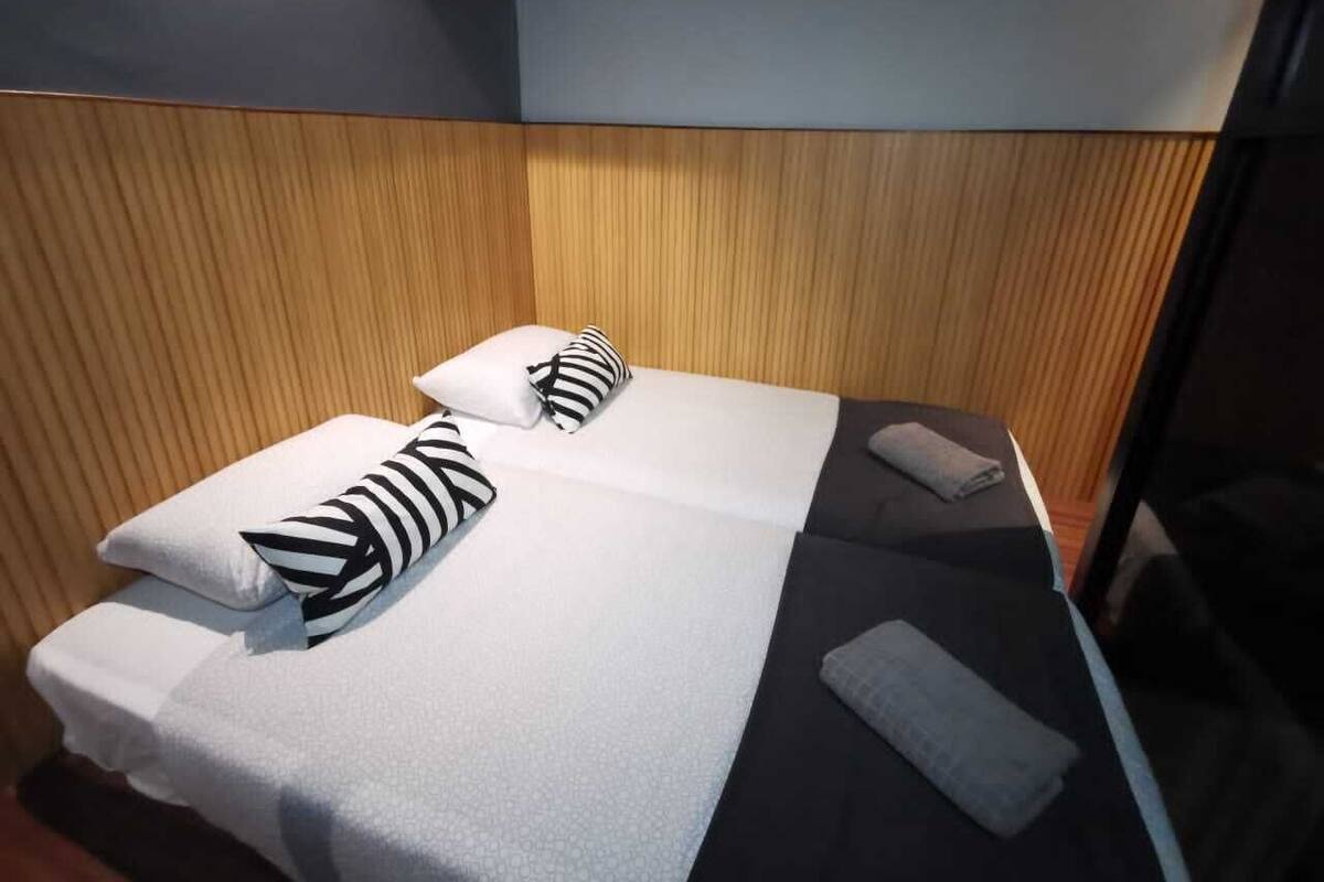 Een tweepersoonsbed met zwart-wit gestreepte kussens, een grijze handdoek en een houten hoofdbord.