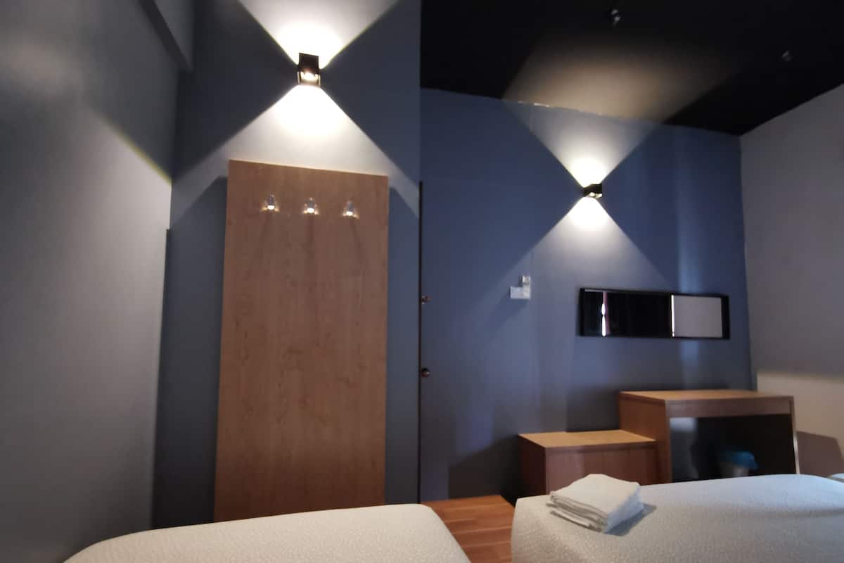 Een hotelkamer met twee bedden, een houten garderobe, een klein bureau en een aan de muur bevestigde televisie.