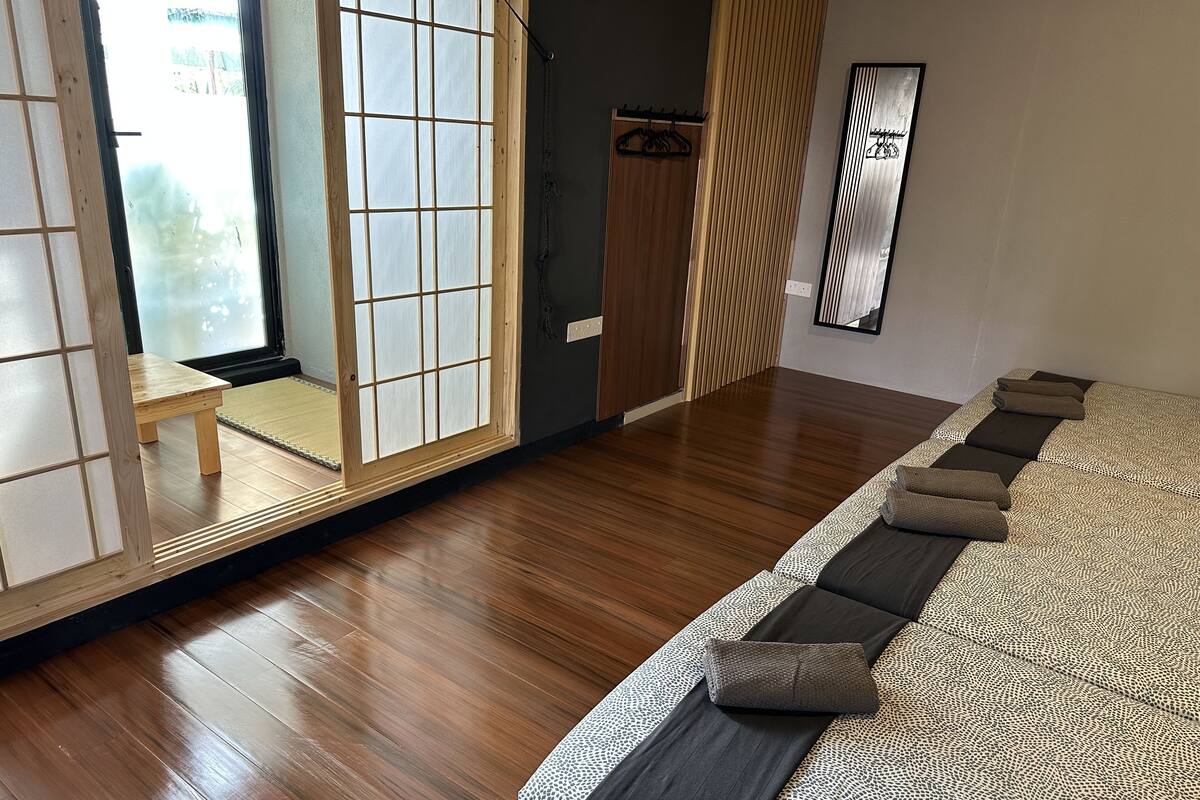 Een kamer met een houten vloer, een bed met beddengoed met een patroon, een schuifdeur en een spiegel aan de muur.