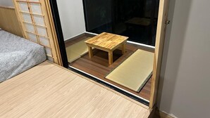 Een kamer met een schuifdeur naar een balkon, een klein houten tafeltje en een tatami mat.