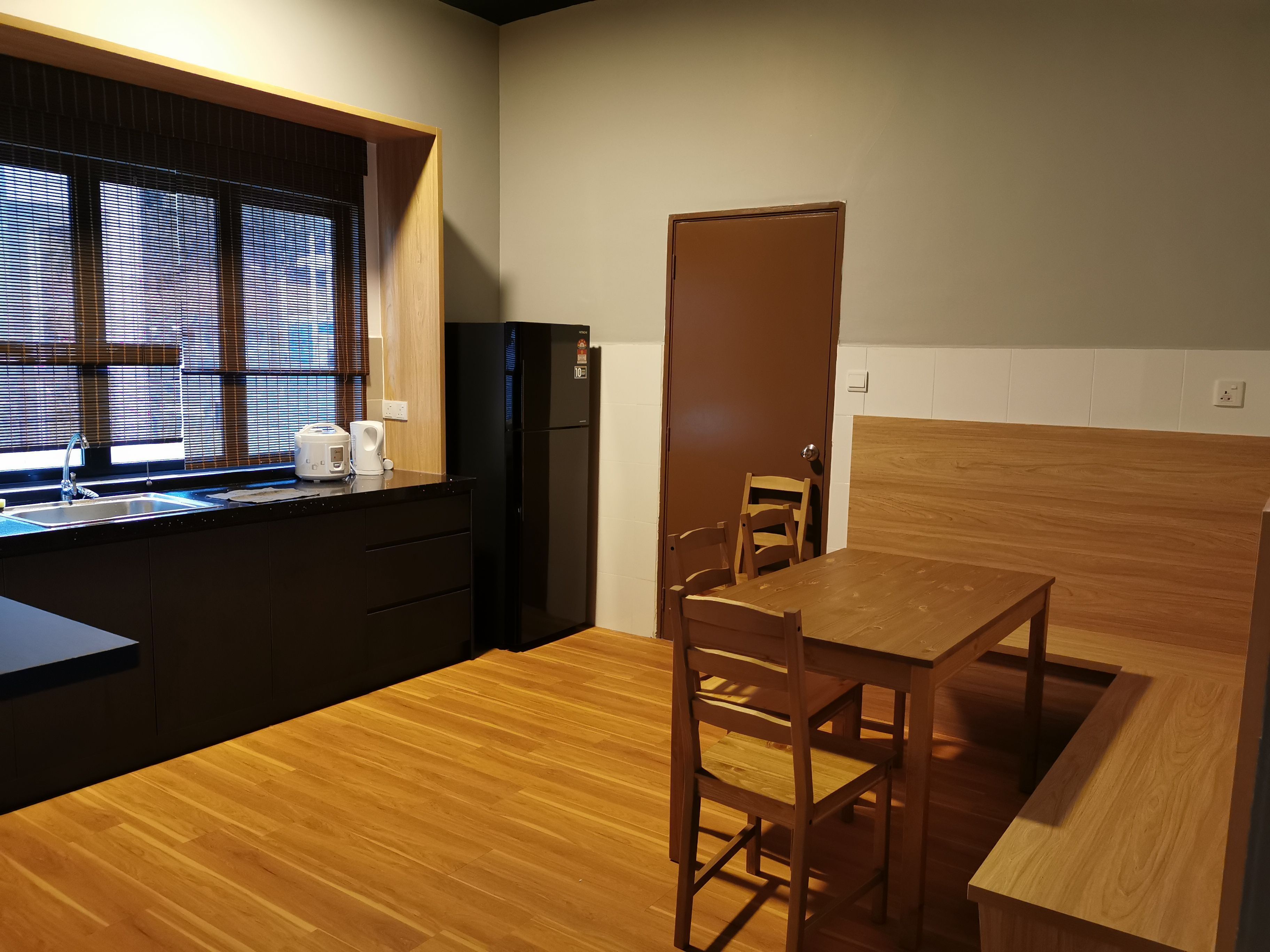 A compact kitchen with a wooden table and chairs, a black refrigerator, and a window with blinds.