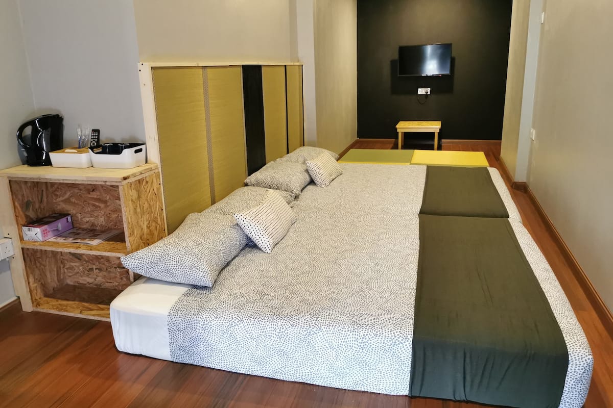 Een kamer met een bed, een houten plank met een waterkoker, een kleine tafel en een aan de muur bevestigde televisie.