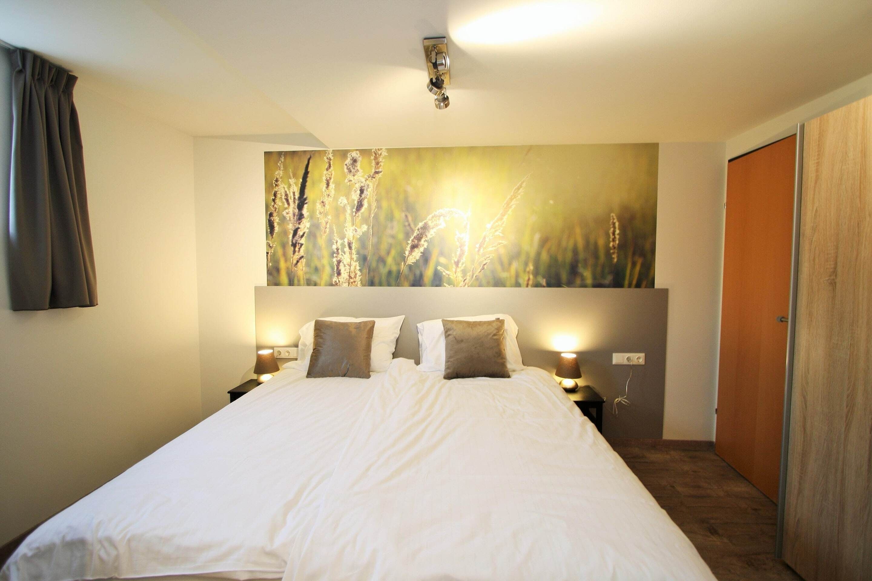 Habitación de hotel con una cama grande, dos lámparas de noche, un cuadro en la pared y una puerta de madera.