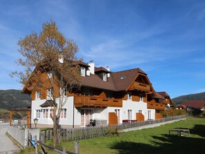 Traditional chalet-style building with multiple windows and balconies, situated in a serene rural setting surrounded by lush greenery.