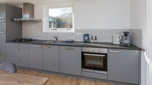 A modern kitchen with grey cabinets, a built-in oven, a coffee maker, and a window overlooking a garden. - Holiday Home Near Veerse Meer Lake Wolphaartsdijk (Wolphaartsdijk)
