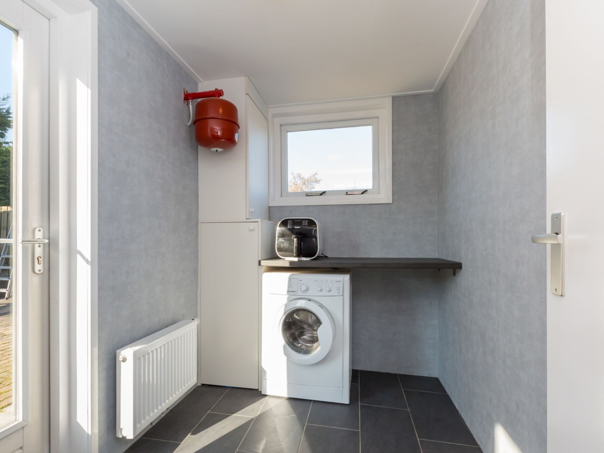A compact laundry area with a washing machine, a small window, and a red water heater.