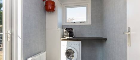 A compact laundry area with a washing machine, a small window, and a red water heater.