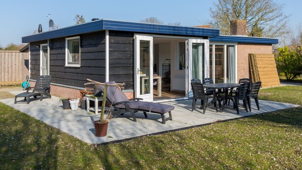 A small, single-story house with a patio area featuring outdoor furniture and a potted plant. - Holiday Home Near Veerse Meer Lake Wolphaartsdijk (Wolphaartsdijk)