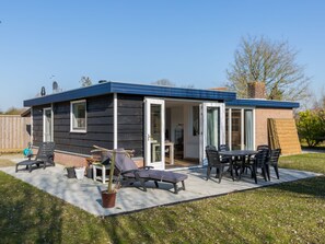 Ein kleines, eingeschossiges Haus mit einer Terrassenanlage, die Gartenmöbel und einen Blumentopf zeigt.