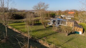 A modern house with a large glass conservatory, surrounded by a well-maintained lawn and trees. - Holiday Home Near Veerse Meer Lake Wolphaartsdijk (Wolphaartsdijk)