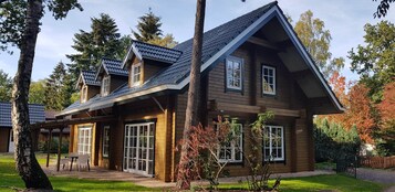 A two-story wooden house with a sloped roof, large windows, and a covered patio area.