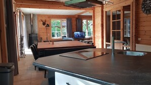 Et interiør af en træhytte med et køkkenområde, der inkluderer en sort bordplade, en vask og et spisebord med stole.