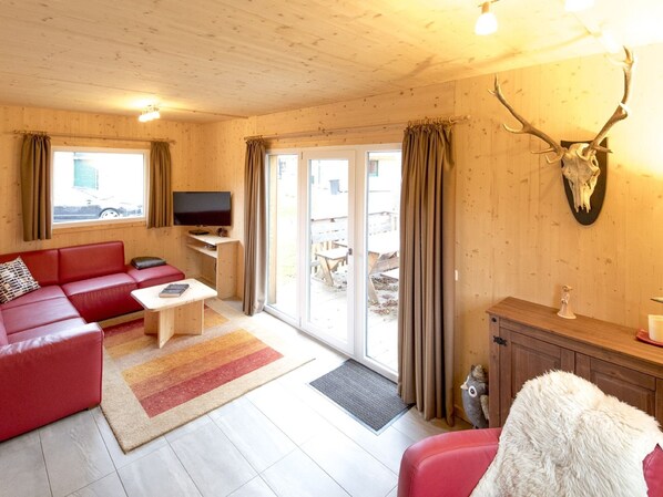 L’intérieur d’un chalet chaleureux, avec un canapé rouge, un téléviseur et un crâne de cerf accroché au mur.