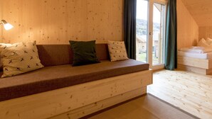 Una habitación de cabaña acogedora con interior de madera, un sofá con cojines estampados, una cama y una ventana con cortinas.