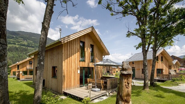 Una cabaña de madera con terraza, rodeada de árboles y un área con césped.