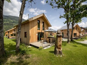 Une cabane en bois dotée d’une terrasse, entourée d’arbres et d’une zone herbeuse.
