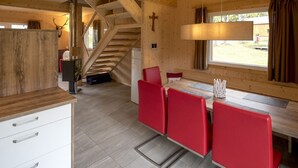 Un interior de madera con una zona de comedor que incluye sillas rojas y una mesa. Se ve una escalera al fondo.