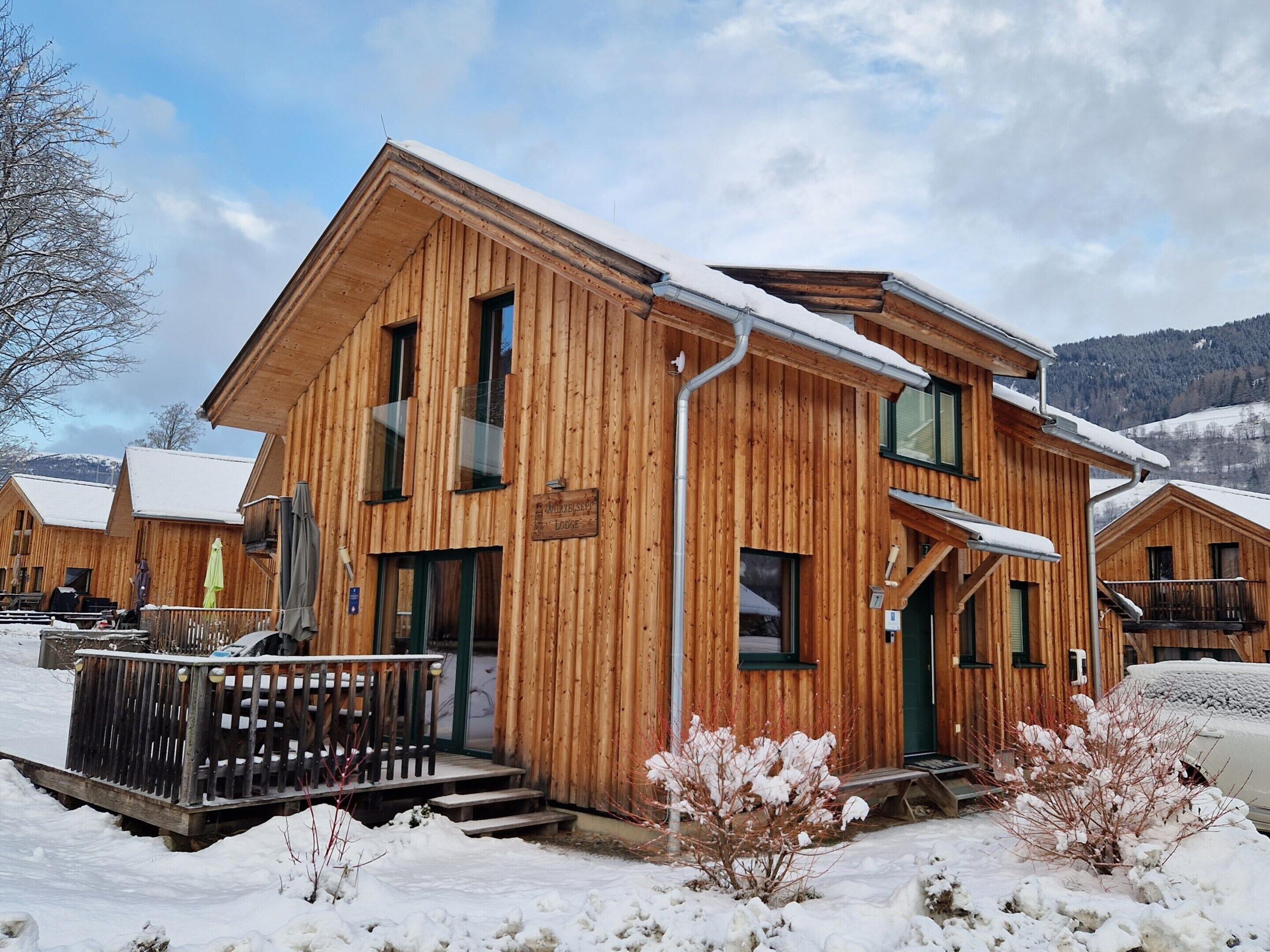 Een houten lodge met een sneeuwbedekte dak, een houten terras en een bord waarop staat dat het een lodge is.