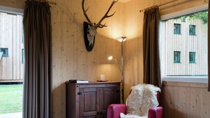 Un interior de madera con un cráneo de ciervo montado en la pared, una silla roja con un plaid de piel y un escritorio con una lámpara.