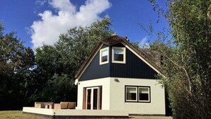 A two-story house with a dark roof, light-colored walls, and a small porch with seating. - Mansion in De Cocksdorp (De Cocksdorp)
