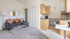A compact living space with a kitchenette, a sofa with cushions, a coffee table, and a mirror. - Balfour · Stylish and Comfortable City Centre Apartment (Edinburgh)