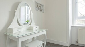 A white vanity with a glass top, two drawers, and a large mirror. There is a framed picture on the wall above the vanity. - Balfour · Stylish and Comfortable City Centre Apartment (Edinburgh)