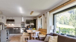 A modern kitchen with stainless steel appliances, a dining area with a wooden table and bench, and a large window offering a view of a forested area. - Leogang Chalet Near Ski Lift & Bikepark (Leogang)