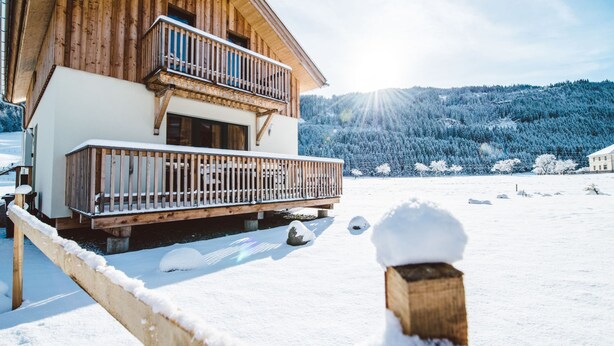 Een houten chalet met balkon, omgeven door een besneeerd landschap en bomen.